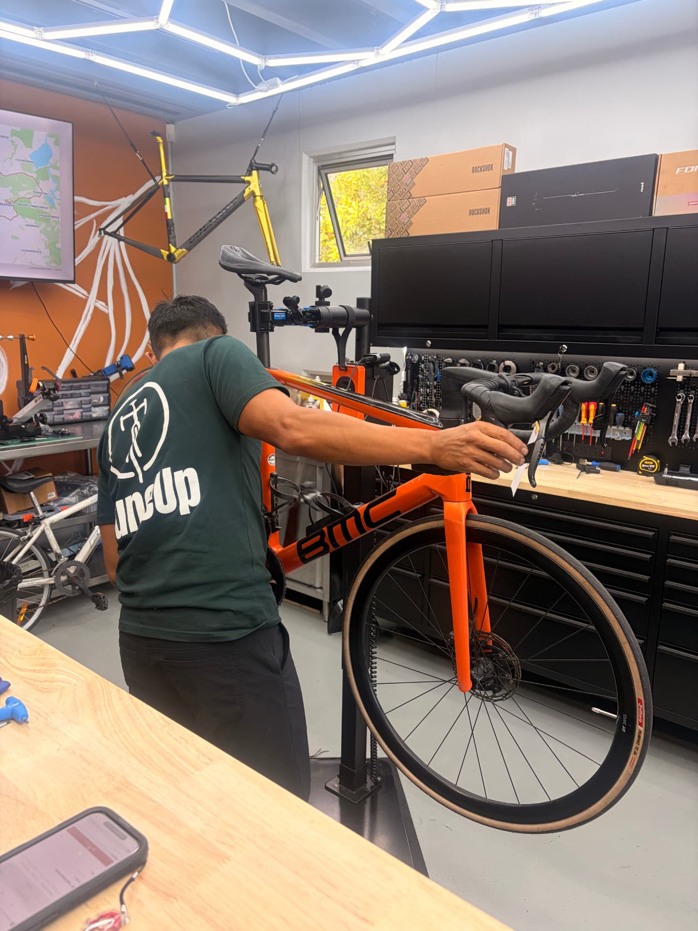 TuneUp Cycles mechanic working on an orange BMC road bike in the Noosaville workshop